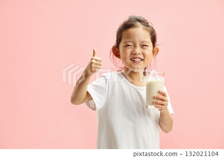 Happy Smiling Little Brunette Child Girl Drinking Milk From Glass With a Trace Frm Milk on Lips, Expresses Pleasure Positively Showing Thumb up Standing On Pink Isolated Happy Smiling Little Brunette Child Girl Drinking Milk From Glass With a Trace Frm Milk on Lips, Expresses Pleasure Positively Showing Thumb up Standing On Pink Isolated 132021104