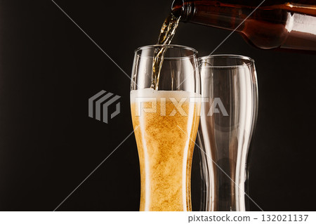 Pouring beer into glasses from bottle on dark. Pouring beer into glasses from bottle on dark. 132021137