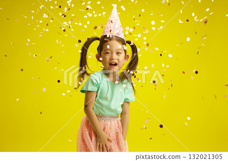 Cheerful Asian Child Girl Celebrating Birthday with Confetti on Yellow Isolated Background 132021305