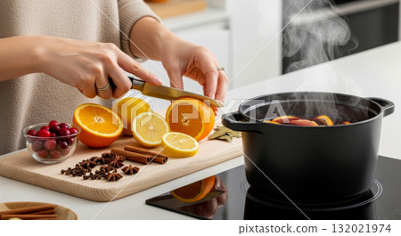 Woman cutting an orange for steaming mulled wine with cloves, cinnamon, and star anise. Cozy winter drink preparation. Woman cutting an orange for steaming mulled wine with cloves, cinnamon, and star anise. Cozy winter drink preparation. 132021974