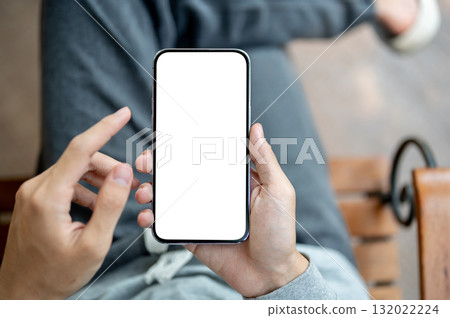 A hand holding smartphone with finger pointing at white screen, sitting cross legged on chair. A hand holding smartphone with finger pointing at white screen, sitting cross legged on chair. 132022224