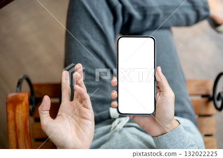 A hand holding white screen smartphone with other hand in explaining gesture, sitting cross legged. A hand holding white screen smartphone with other hand in explaining gesture, sitting cross legged. 132022225