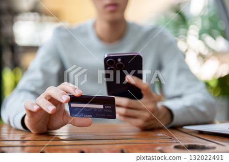 A man holding smartphone and other holding a credit card while sitting at wooden table in cafe. 132022491