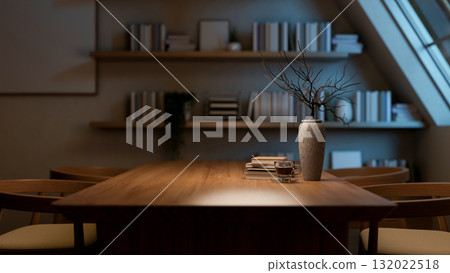 A coffee cup on wooden table and armchairs next to a bookshelf in a dim room with roof window. A coffee cup on wooden table and armchairs next to a bookshelf in a dim room with roof window. 132022518