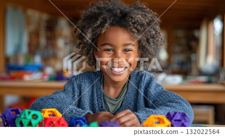 A cheerful young child with a curly afro smiles at the camera while playing with colorful geometric blocks at a table, radiating joy and childhood innocence A cheerful young child with a curly afro smiles at the camera while playing with colorful geometric blocks at a table, radiating joy and childhood innocence 132022564