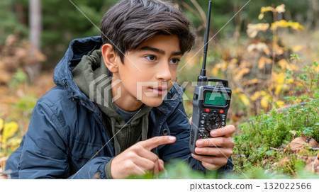 A young boy explores in nature using a handheld transceiver to communicate, his gaze is fixed on the walkie-talkie as he navigates through the outdoor environment 132022566