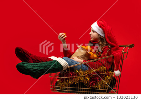 Girl in Santa hat sitting in shopping cart holding oranges. Girl in Santa hat sitting in shopping cart holding oranges. 132023130