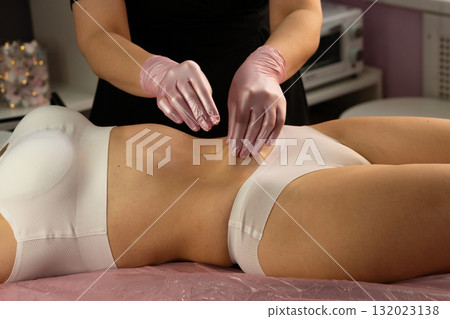 Aesthetician performs abdominal massage wearing pink protective gloves. Aesthetician performs abdominal massage wearing pink protective gloves. 132023138