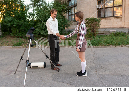 Man and woman shake hands near telescope outdoors Man and woman shake hands near telescope outdoors 132023146
