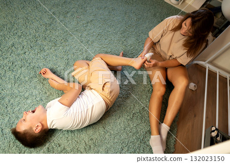 Mother helping laughing boy with socks on carpet 132023150