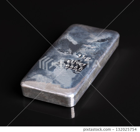 Cast silver bar, side view on black glass plate and background. Silver ingot with an irregular surface created by the cooling of the liquid metal. Stamped with 1 kg for the weight, and 999,0 purity. Cast silver bar, side view on black glass plate and background. Silver ingot with an irregular surface created by the cooling of the liquid metal. Stamped with 1 kg for the weight, and 999,0 purity. 132025754