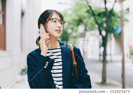 一名年輕女子一邊打電話一邊走在街上 132025873