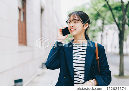 一名年輕女子一邊打電話一邊走在街上 132025874