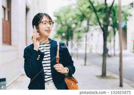 一名年輕女子一邊打電話一邊走在街上 132025875