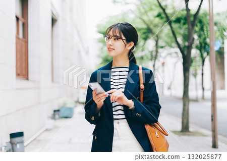 一位年輕女子一邊看著智慧型手機一邊尋找商店 一位年輕女子一邊看著智慧型手機一邊尋找商店 132025877