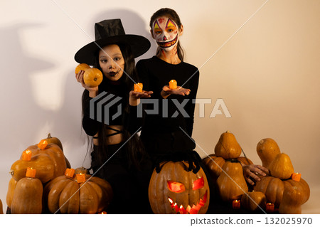 Two girls in Halloween costumes are posing with pumpkins and candles 132025970