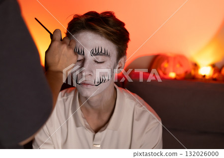 A person is getting their face painted with a skeleton design for a Halloween  132026000