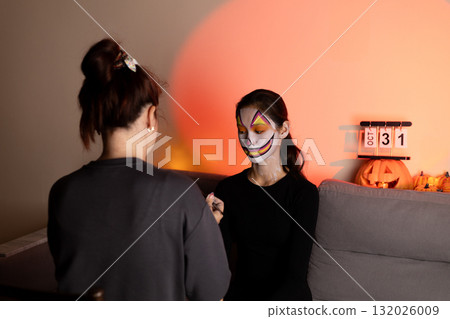 One person is getting their face painted for Halloween, while another person 132026009