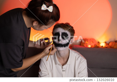 A person is applying skull makeup to another person's face for Halloween 132026010