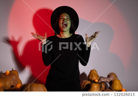 The witch is casting a spell with her hands raised surrounded by pumpkins. The witch is casting a spell with her hands raised surrounded by pumpkins. 132026013