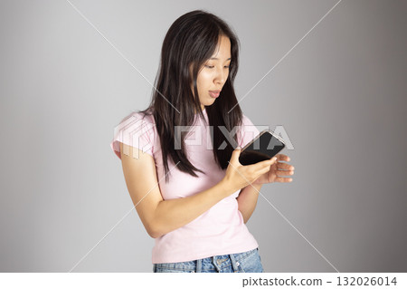 The woman is looking at her smartphone with a surprised expression The woman is looking at her smartphone with a surprised expression 132026014