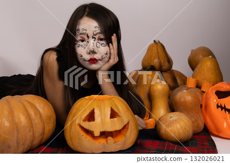 Woman with painted face surrounded by pumpkins, creating a festive Woman with painted face surrounded by pumpkins, creating a festive 132026021