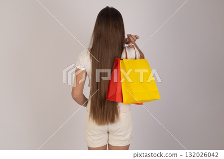 Woman with long hair holding yellow and red shopping bag. 132026042