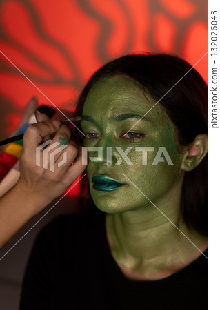 A person is getting their face painted green for a Halloween costume A person is getting their face painted green for a Halloween costume 132026043
