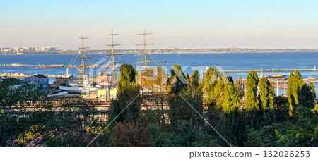 Panoramic view of a coastal harbor in Odessa, Ukraine, featuring tall ships with masts visible above the tree line in the foreground. Panoramic view of a coastal harbor in Odessa, Ukraine, featuring tall ships with masts visible above the tree line in the foreground. 132026253
