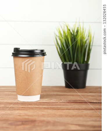 Disposable coffee cup standing on wooden table with decorative plant in background 132026455