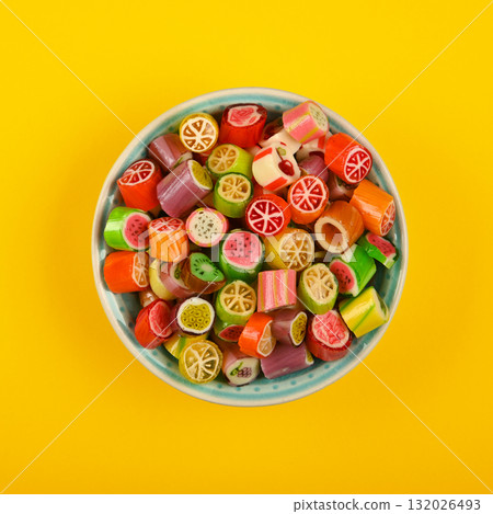 Colorful fruit candies filling a bowl on a yellow background Colorful fruit candies filling a bowl on a yellow background 132026493