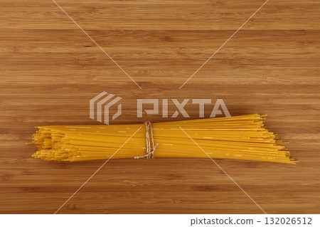 Bunch of raw spaghetti tied with string on wooden table Bunch of raw spaghetti tied with string on wooden table 132026512