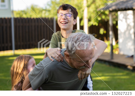 Happy children playing with grandfather in backyard garden on summer holiday 132027223