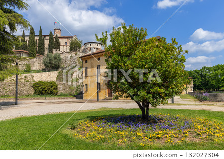 Historic Brescia Castle with Mirabella Tower rises over stone terraces and spring flowers 132027304