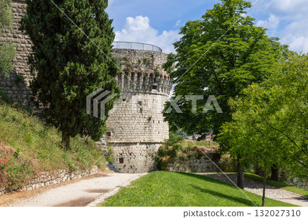 Tower of the French in Brescia Castle stands above sunny garden paths amid green foliage 132027310