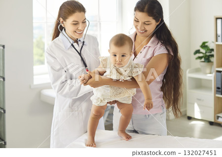 Pediatrician and mother holding baby during clinic checkup, stethoscope assessment Pediatrician and mother holding baby during clinic checkup, stethoscope assessment 132027451