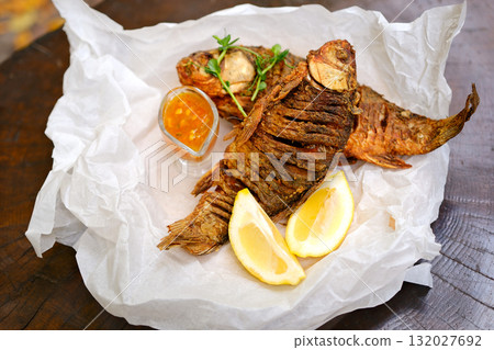 Fried fish lemons Fried whole fish with tomato and onion salad, on black background 132027692