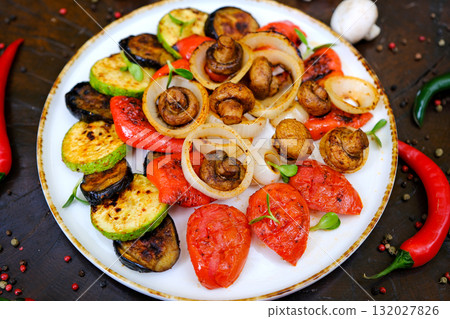 Grilled vegetables: red and yellow paprika, zucchini, eggplant, mushrooms, tomatoes and onions served on rustic wooden cutting board, white table background, top view 132027826