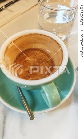 Half-finished cup of espresso on a turquoise saucer with a glass of water in a cozy cafe. Concept of morning routine, simplicity, and the pleasure of everyday coffee moments Half-finished cup of espresso on a turquoise saucer with a glass of water in a cozy cafe. Concept of morning routine, simplicity, and the pleasure of everyday coffee moments 132028205