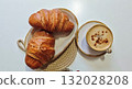 Two golden croissants served on a ceramic plate with a cup of cappuccino sprinkled with cinnamon. Concept of cozy breakfast, comfort, and slow morning indulgence at home or cafe 132028208