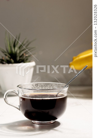 Cup of Dark Coffee With Spoon Sits Beside Plant and Bananas 132028326