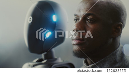 Engineer Next to Glowing AI Robot in Moody, Futuristic Factory Engineer Next to Glowing AI Robot in Moody, Futuristic Factory 132028355