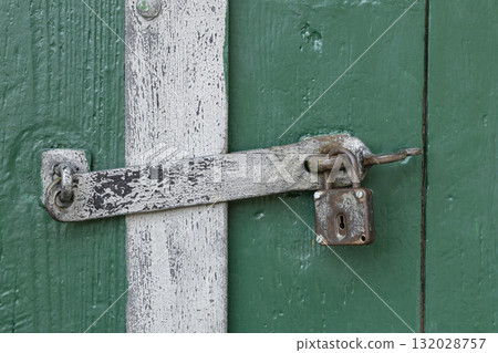 Old metal padlock securing weathered green wooden door Old metal padlock securing weathered green wooden door 132028757