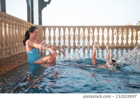 Mother Enjoying Water Play While Child Swims Joyfully Nearby 132028997