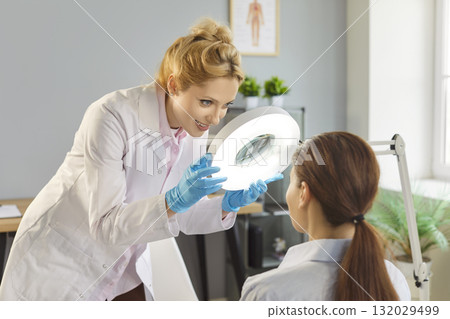 Dermatologist using magnifying lamp for patient skin examination in clinic Dermatologist using magnifying lamp for patient skin examination in clinic 132029499