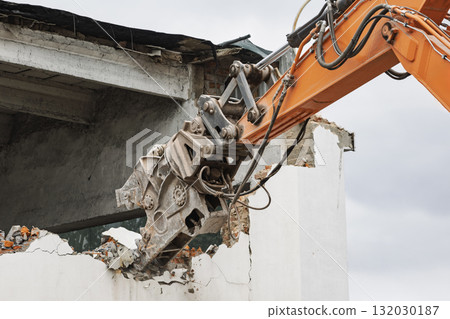Powerful excavator dismantles old building structure in urban demolition project 132030187