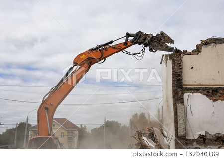 Excavator dismantles a building while debris falls during the demolition process on a cloudy day 132030189