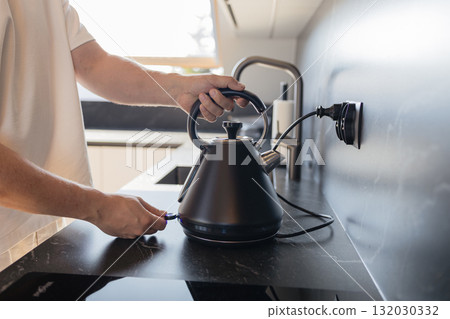 Man placing black electric kettle on modern kitchen stove Man placing black electric kettle on modern kitchen stove 132030332