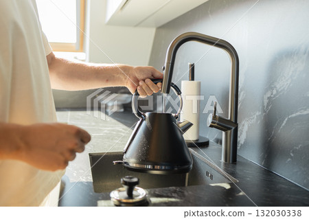 Man filling black kettle with water in modern kitchen sink 132030338