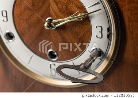 A close-up of a vintage wooden clock face featuring a metal winding key 132030555